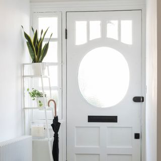 White hallway leading to a white wooden front door with a plant stand next to it