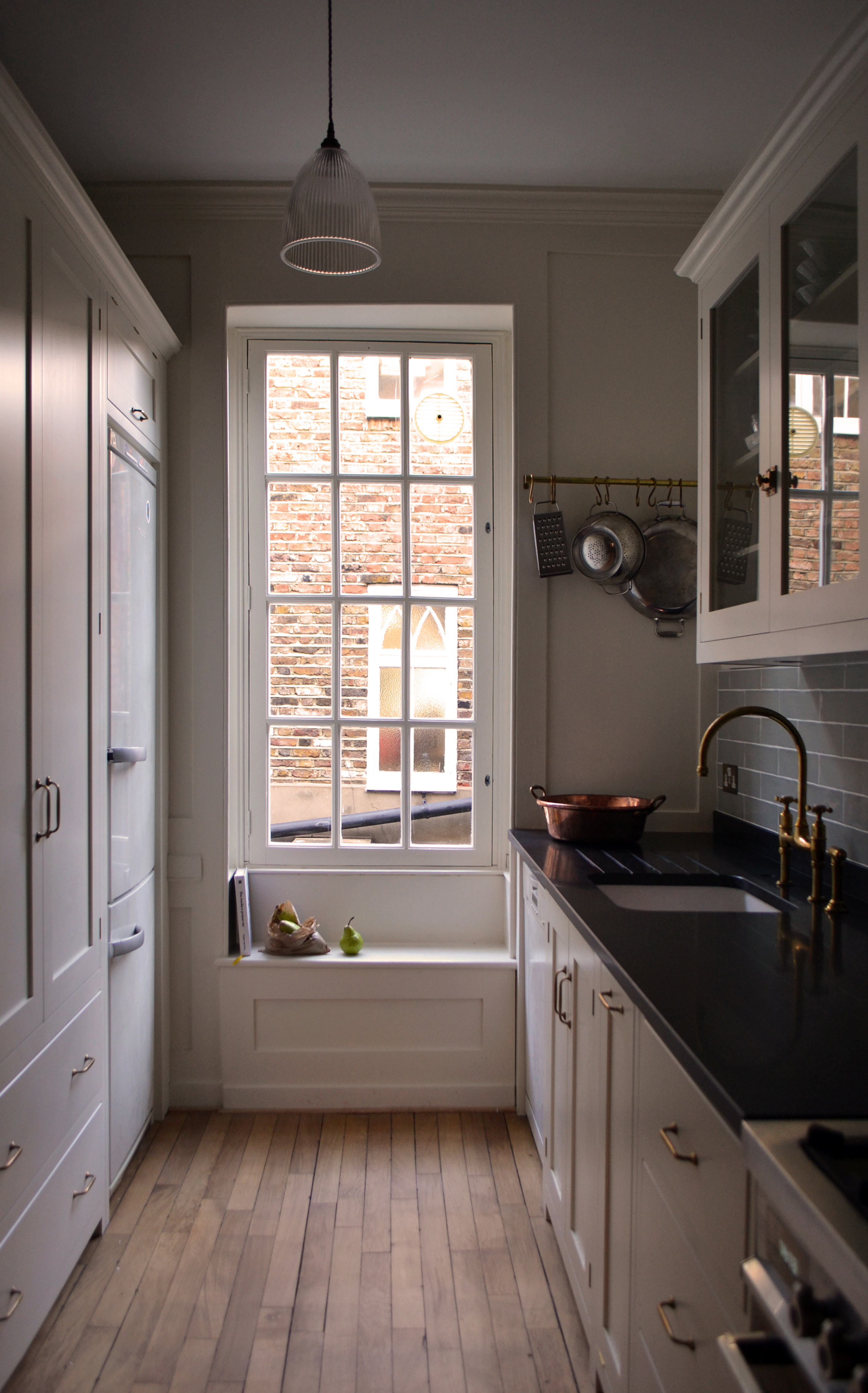 A narrow galley kitchen with white cabinets, and a window seat