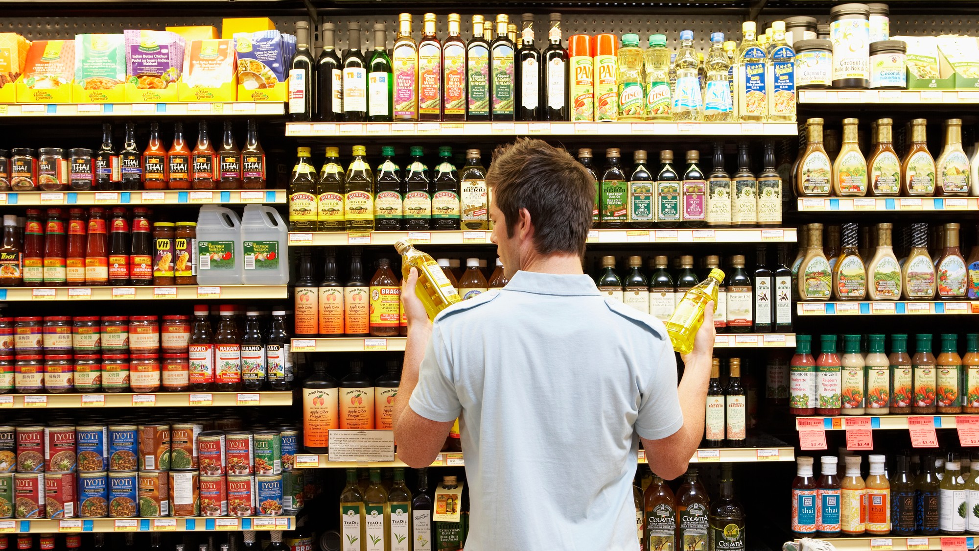 Man in a supermarket comparing bottles of oil
