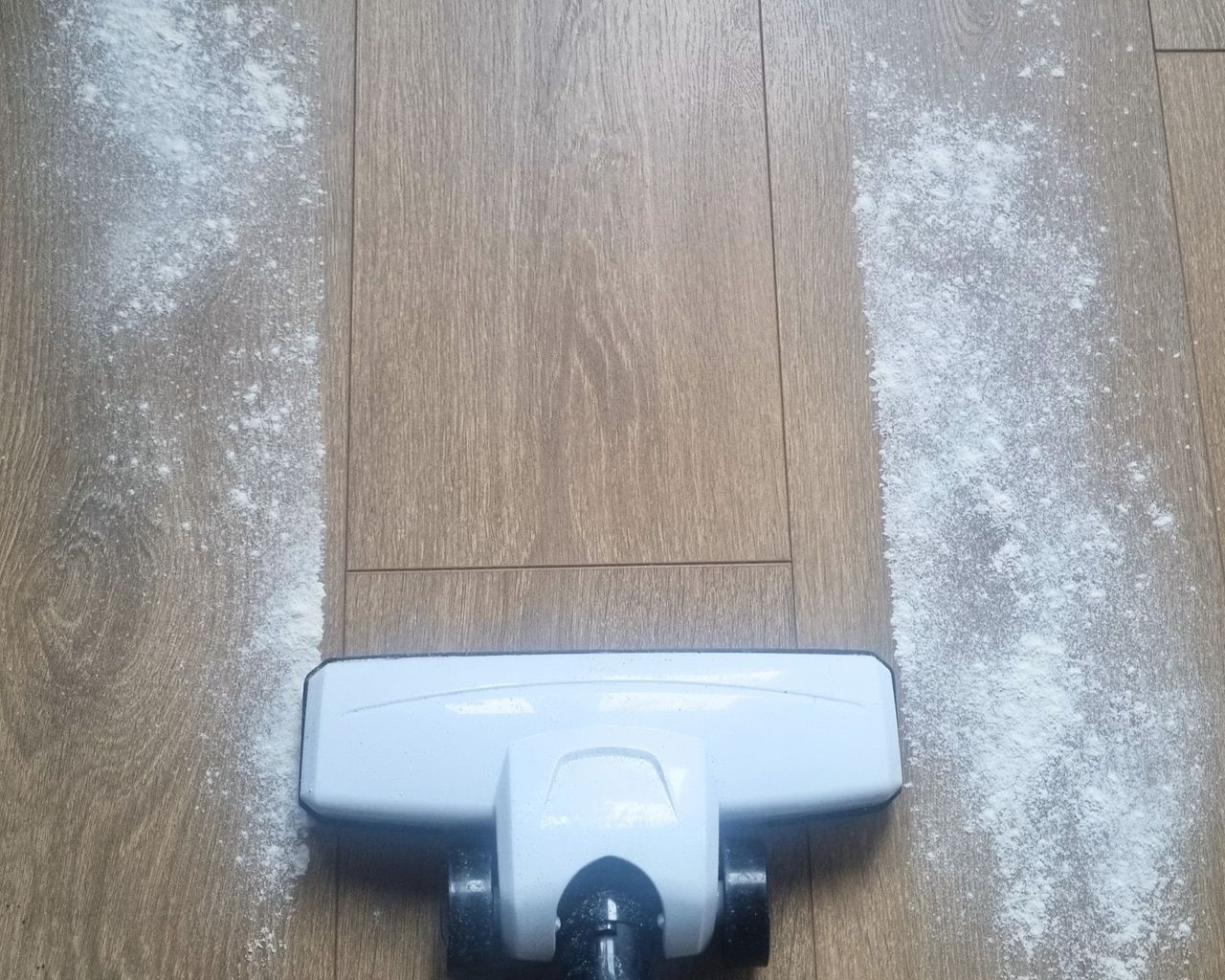 A wooden floor with flour being vacuumed by a white vacuum