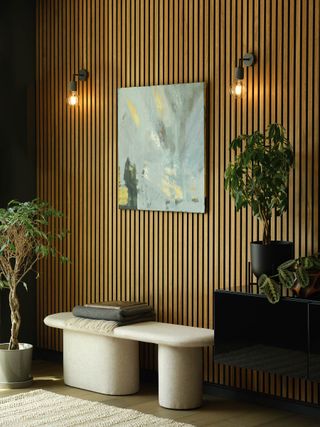 An entryway with wood slat walls, a minimalist bench with warm exposed bulb wall lights either side