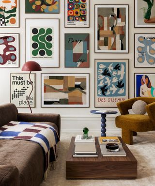 A retro style living room with a gallery wall of colorful prints, a brown couch with a checkered throw, a low wooden coffee table, and a light brown armchair