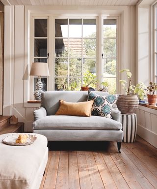A long and narrow living room with wooden floorboard decor, upholstered loveseat and cream framed window