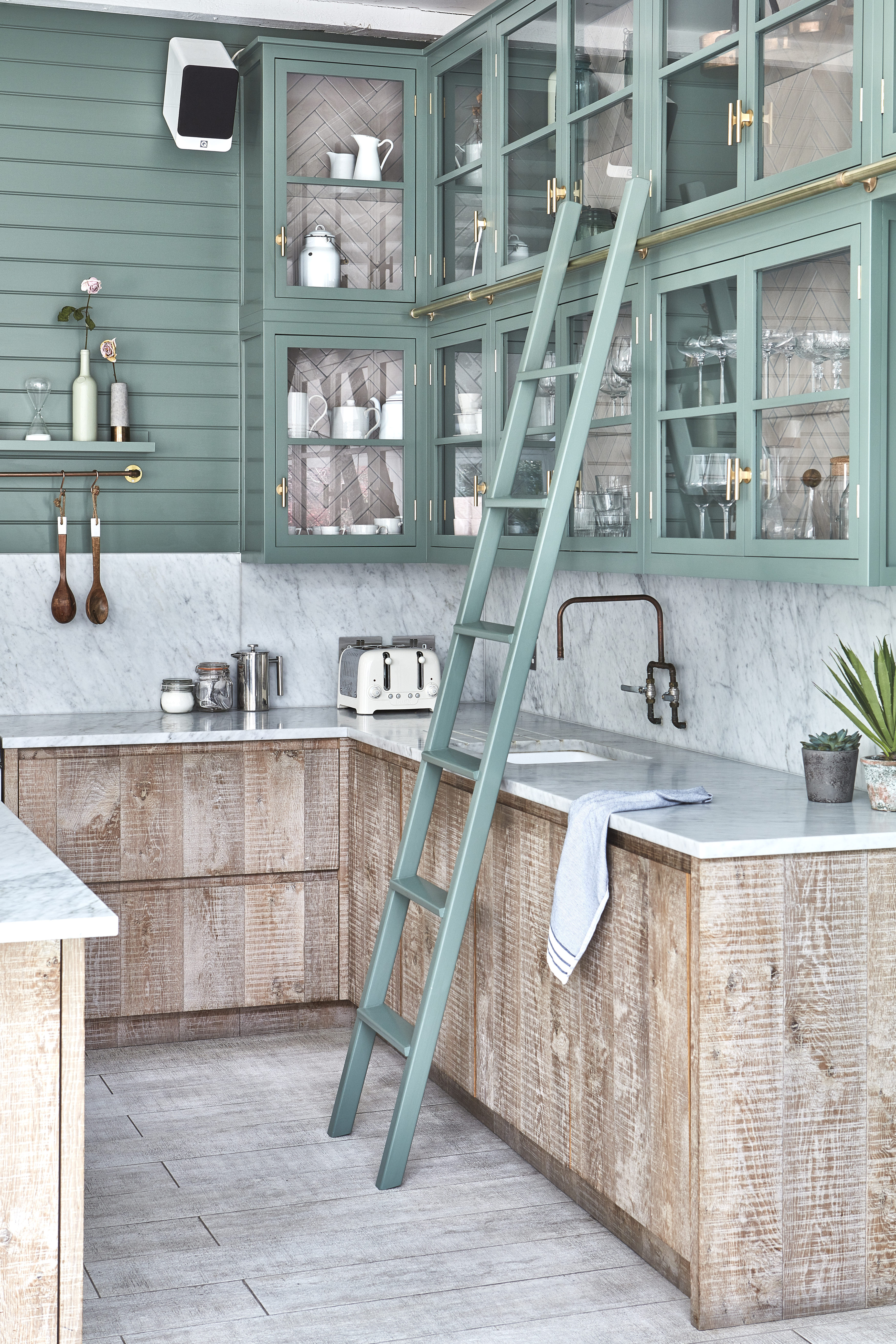 A small kitchen with upper mint cabinets and lower wooden cabinets. A ladder also sits by the cabinet sink