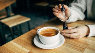 Woman dripping CBD oil into a cappuccino coffee at coffee shop
