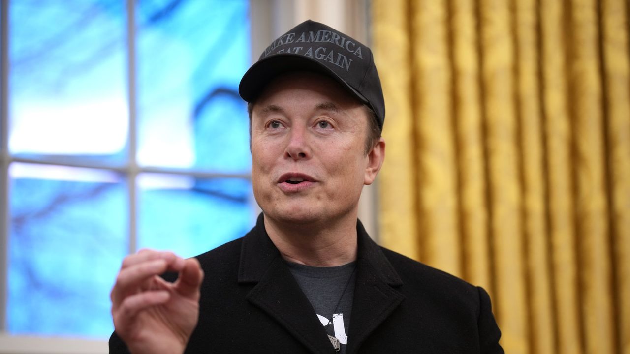 Elon Musk in a black blazer and a black Make America Great Again hat