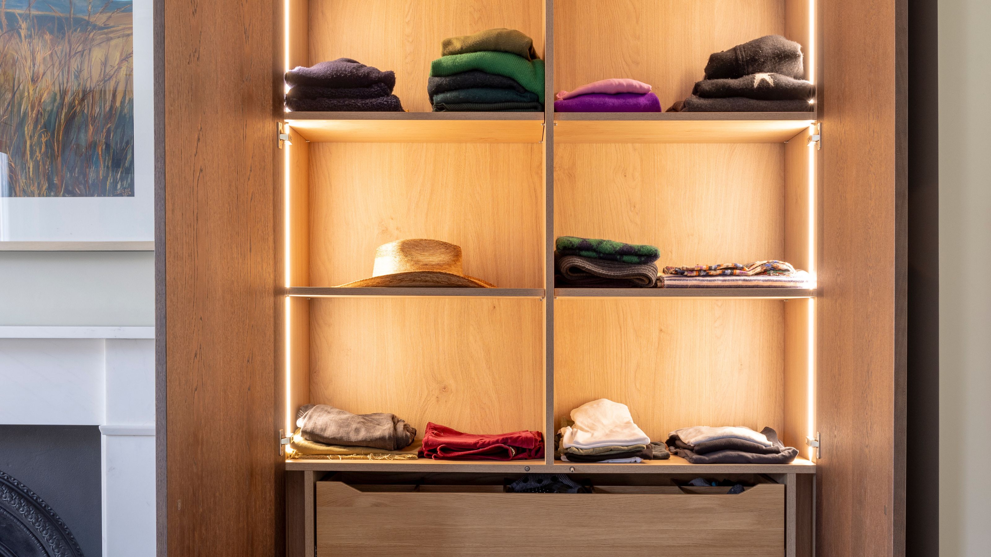 an open wardrobe with timber shelves, under shelf lighting, and jumpers folded on the shelves
