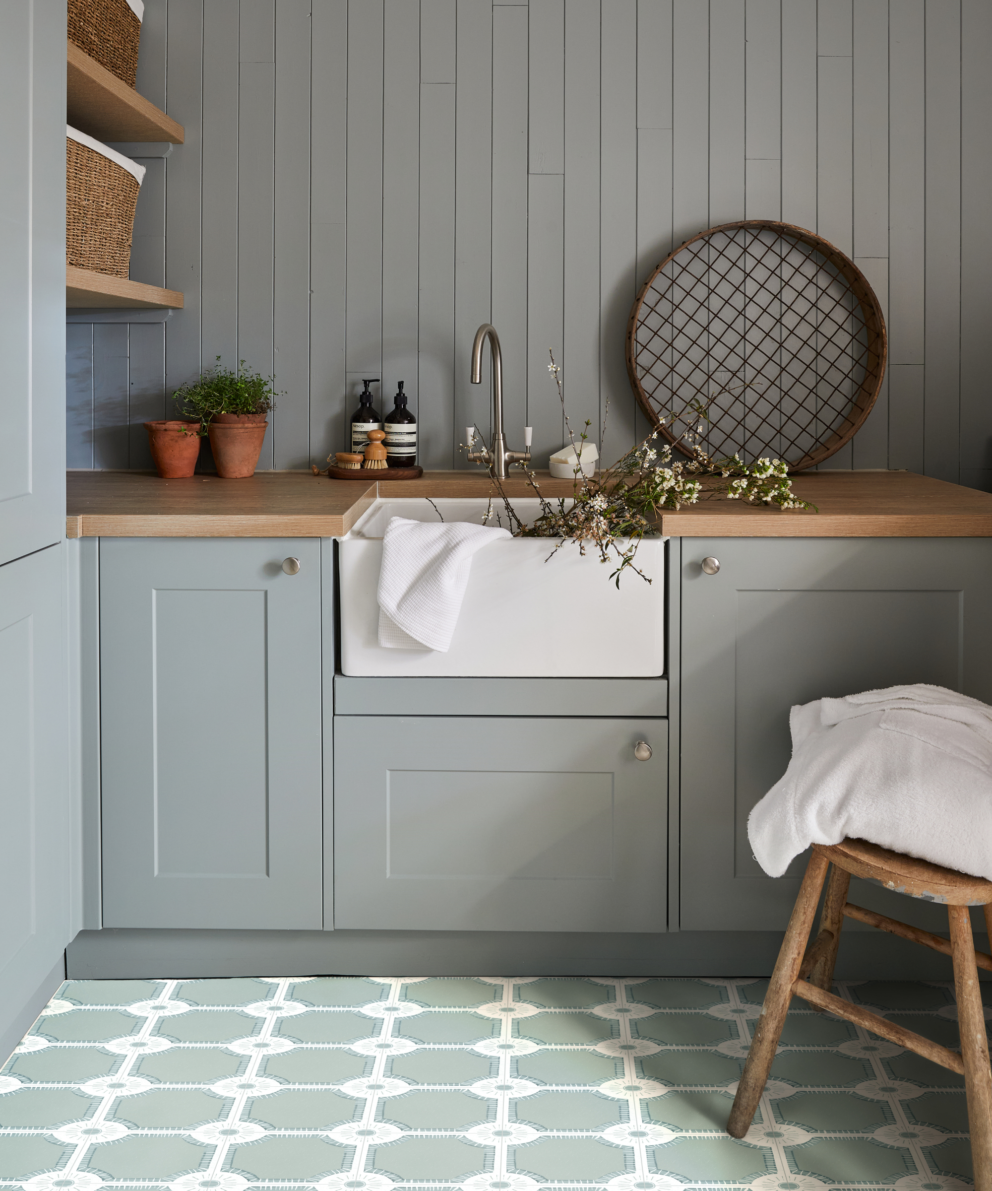 utility room with grey panelled wall, pale duck egg blue units, green and white patterned floor tiles, white butler sink and tap