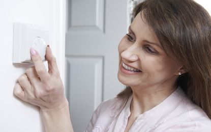 Woman Adjusting Thermostat On Central Heating Control