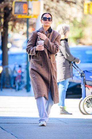 A photo of Katie Holmes styling her brown Reformation coat with gray sweatpants and Adidas sneakers.