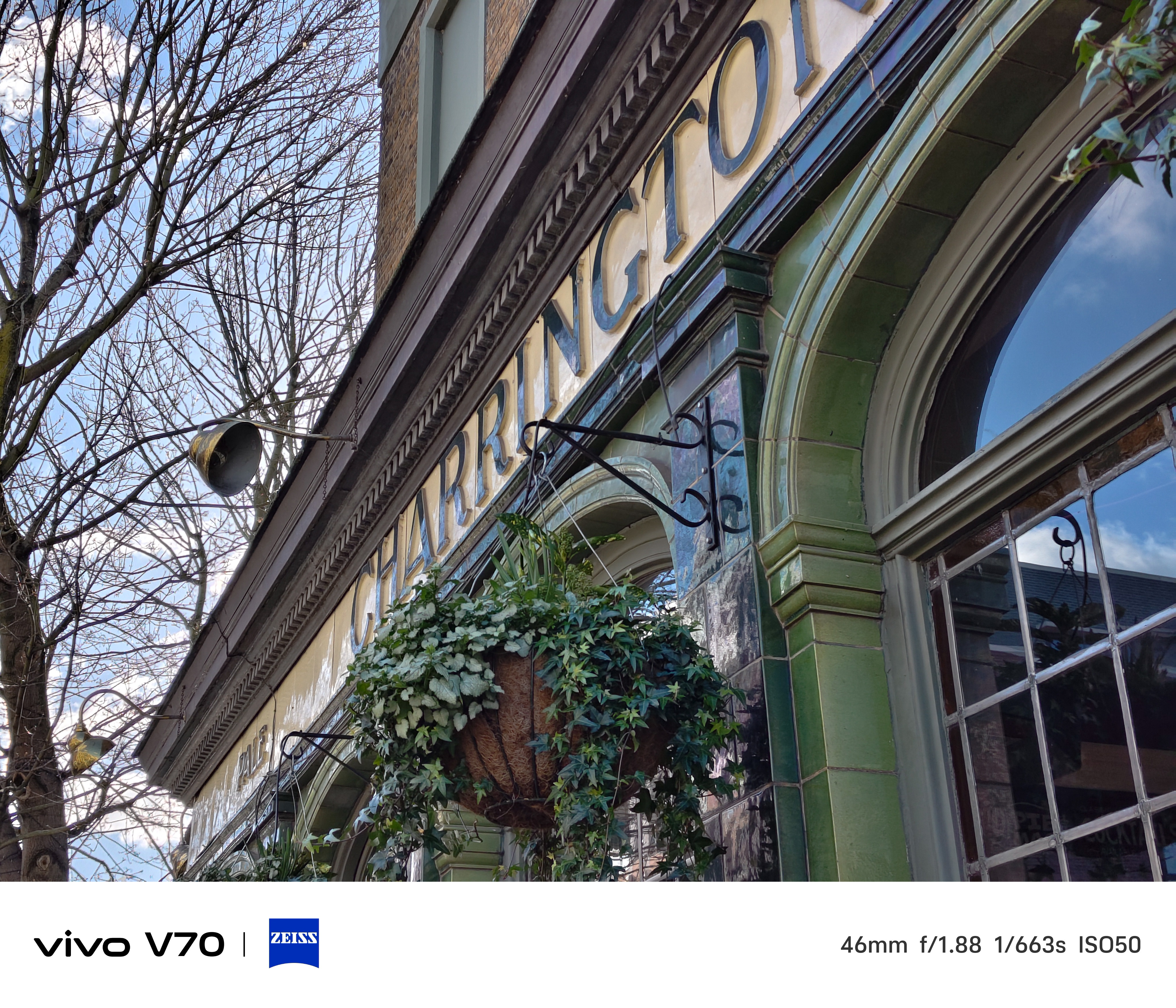 Angled view of green-tiled “CHARRINGTON” pub façade with hanging basket and arched windows.