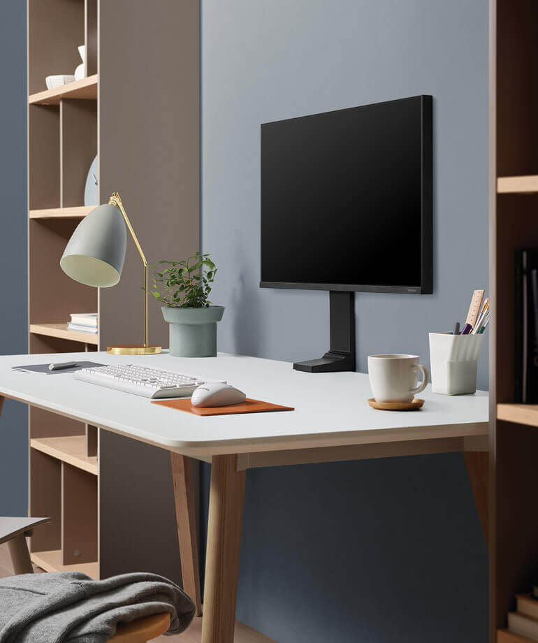 small space monitor by samsung on a wooden desk with a white top, against a blue wall and next to built-in storage units with shelves