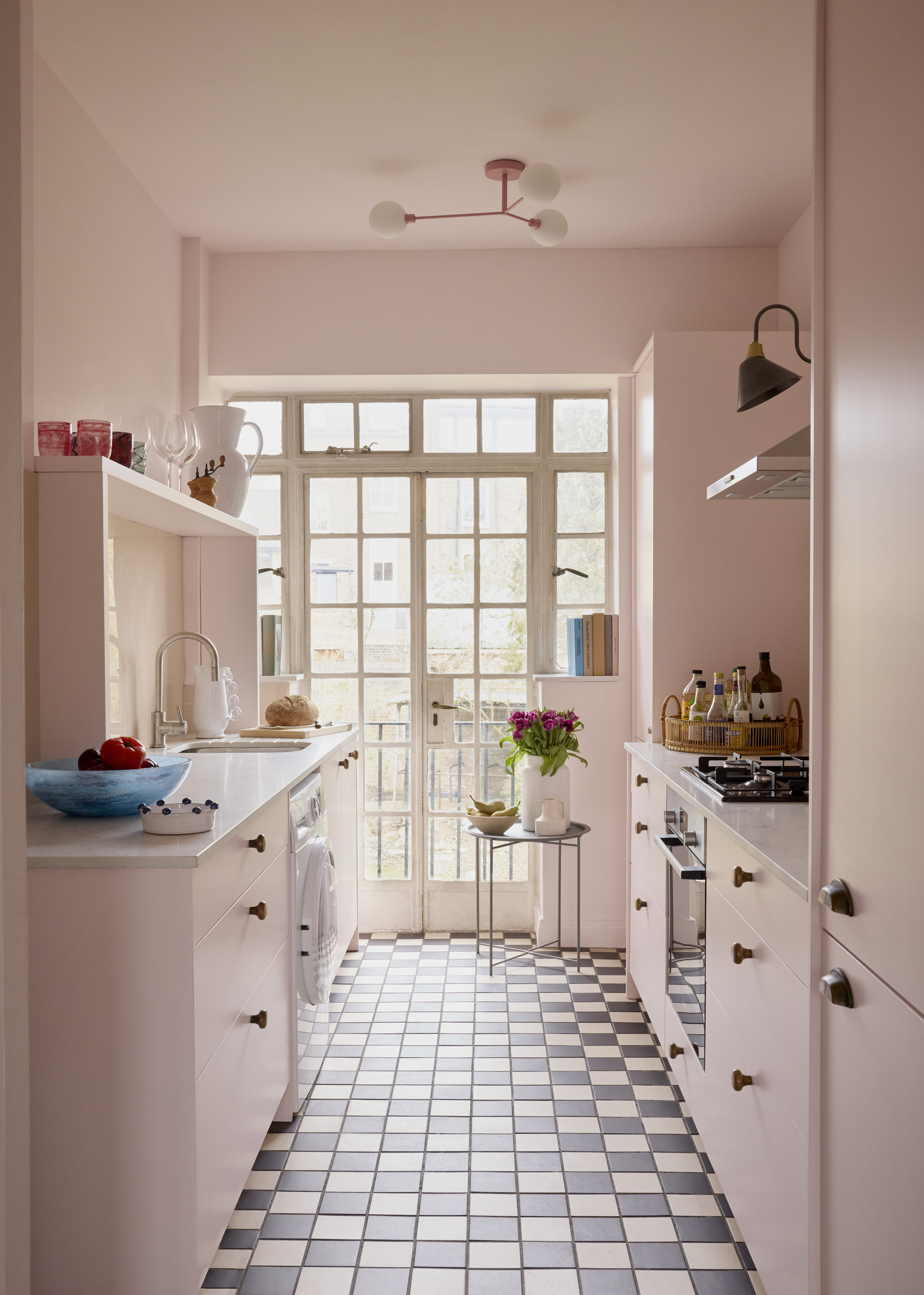 A small kitchen with pale pink walls and cabinetry and black and white checkerboard flooring