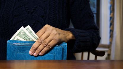A woman holds a wallet with dollar bills sticking out of it.