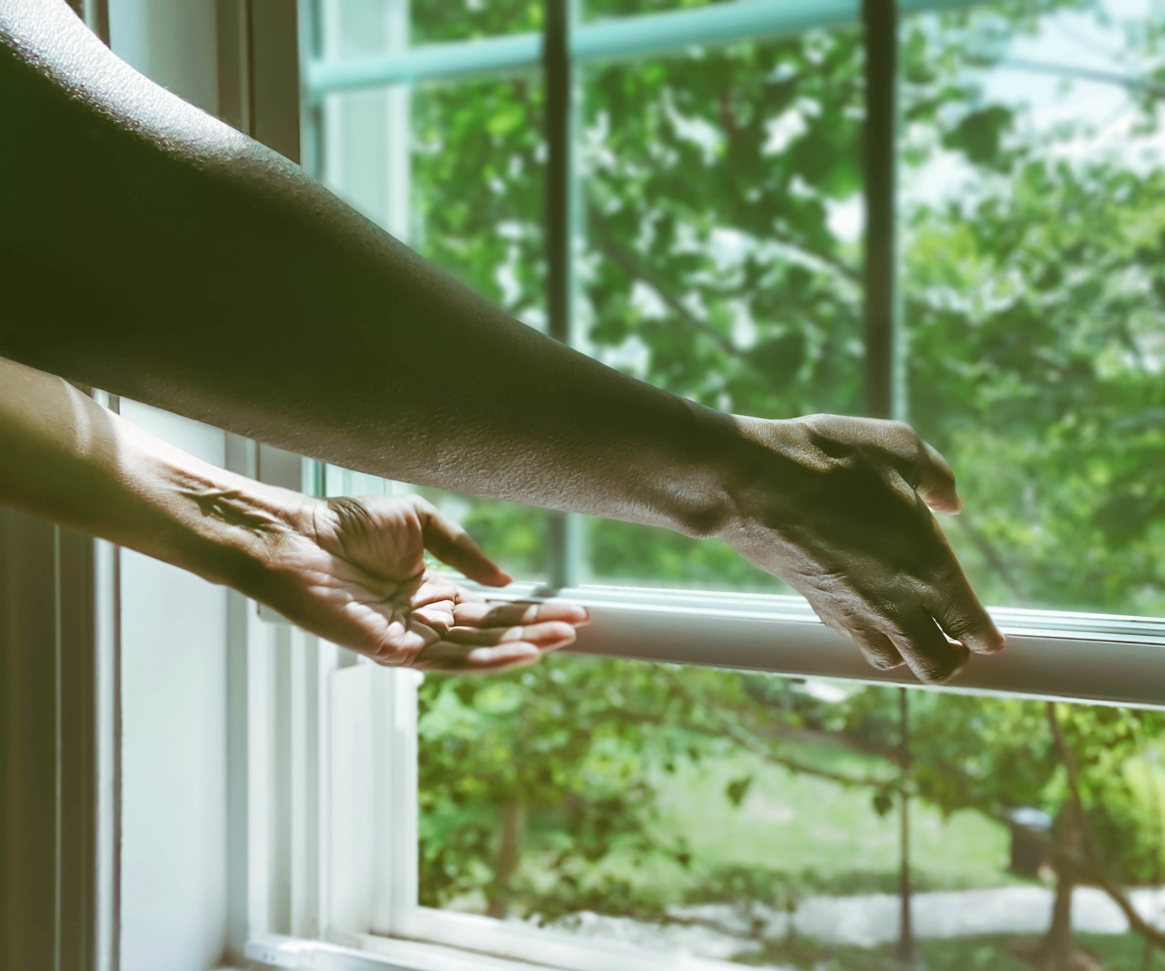 Arms reaching to open a window overlooking green trees