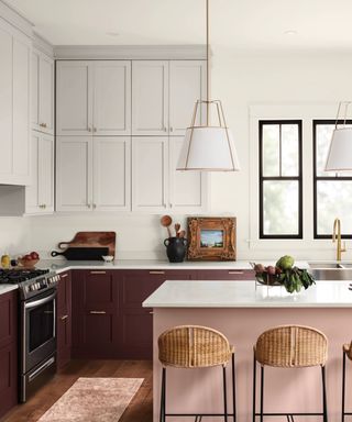 colors that go with light pink, kitchen with pale pink island and dark violet cabinetry, white wall cabinets, hardwood floor, rattan and metal bar stools, white countertops, large pendants