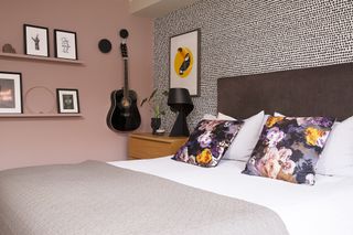 Bedroom with dusty pink walls, a monochrome patterned feature wall, high headboard bed and guitar