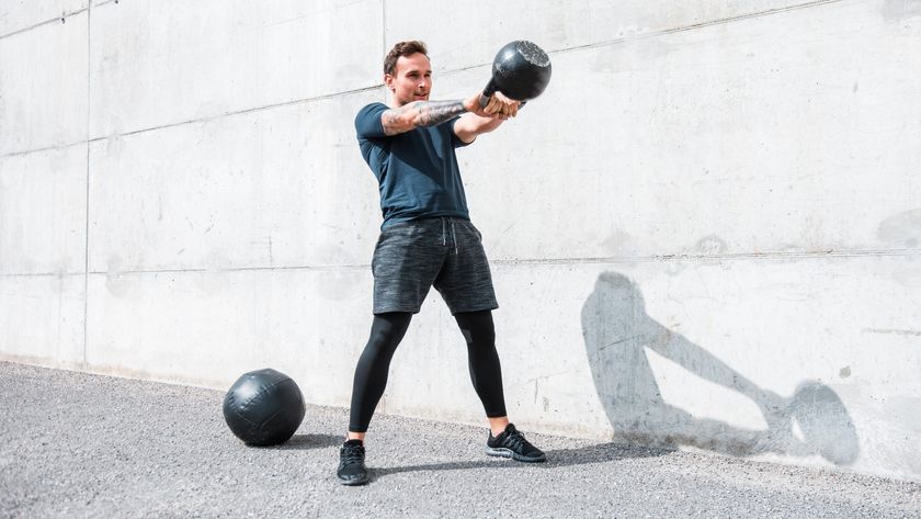 Man performing a kettlebell swing outdoors against a white wall