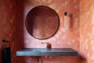 pink powder room with rectangular marble basin, black round mirror, pendant light