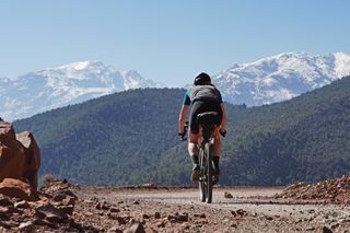 Image shows Anna cycling towards the snow-capped peaks of the Atlas Mountains in Morocco