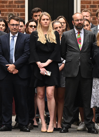 Onlookers, including Charlotte Owen, (C) an aide to Boris Johnson, watch as Prime Minister Boris Johnson addresses the nation to announce his resignation outside 10 Downing Street, on July 7, 2022 in London, England