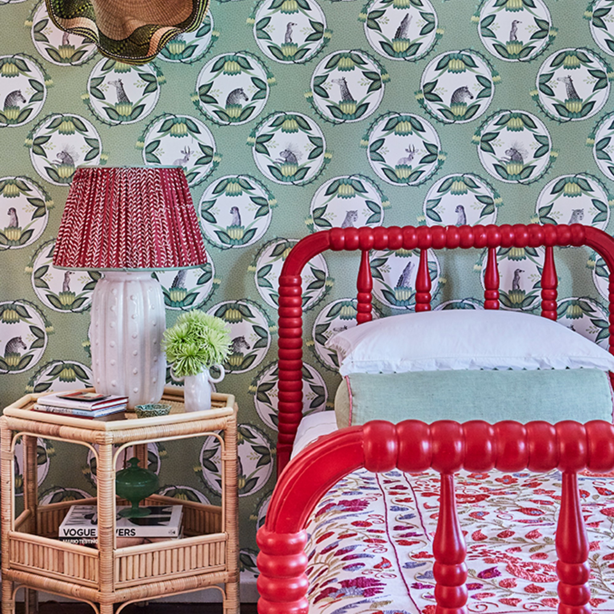 A bedroom with a green patterned wallpaper and a red bobbin bed