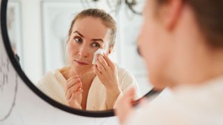 A woman looking into the mirror while applying a facewipe