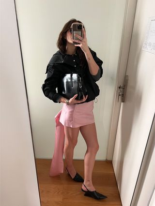 Eliza Huber wearing a black Proenza Schouler technical jacket with a pink Prada satin mini skirt during Milan Fashion Week.