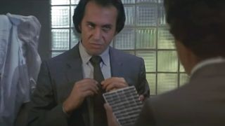 Gene Simmons adjusts his tie with a menacing face in Runaway.