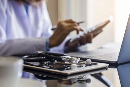 doctor using calculator, working on laptop, with stethoscope and tablet