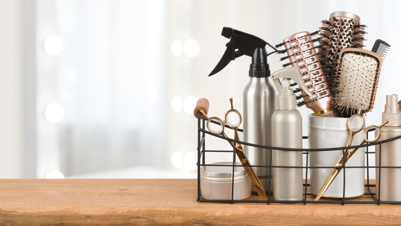 Side view of a basket of hair products and styling tools sat on a wooden surface 