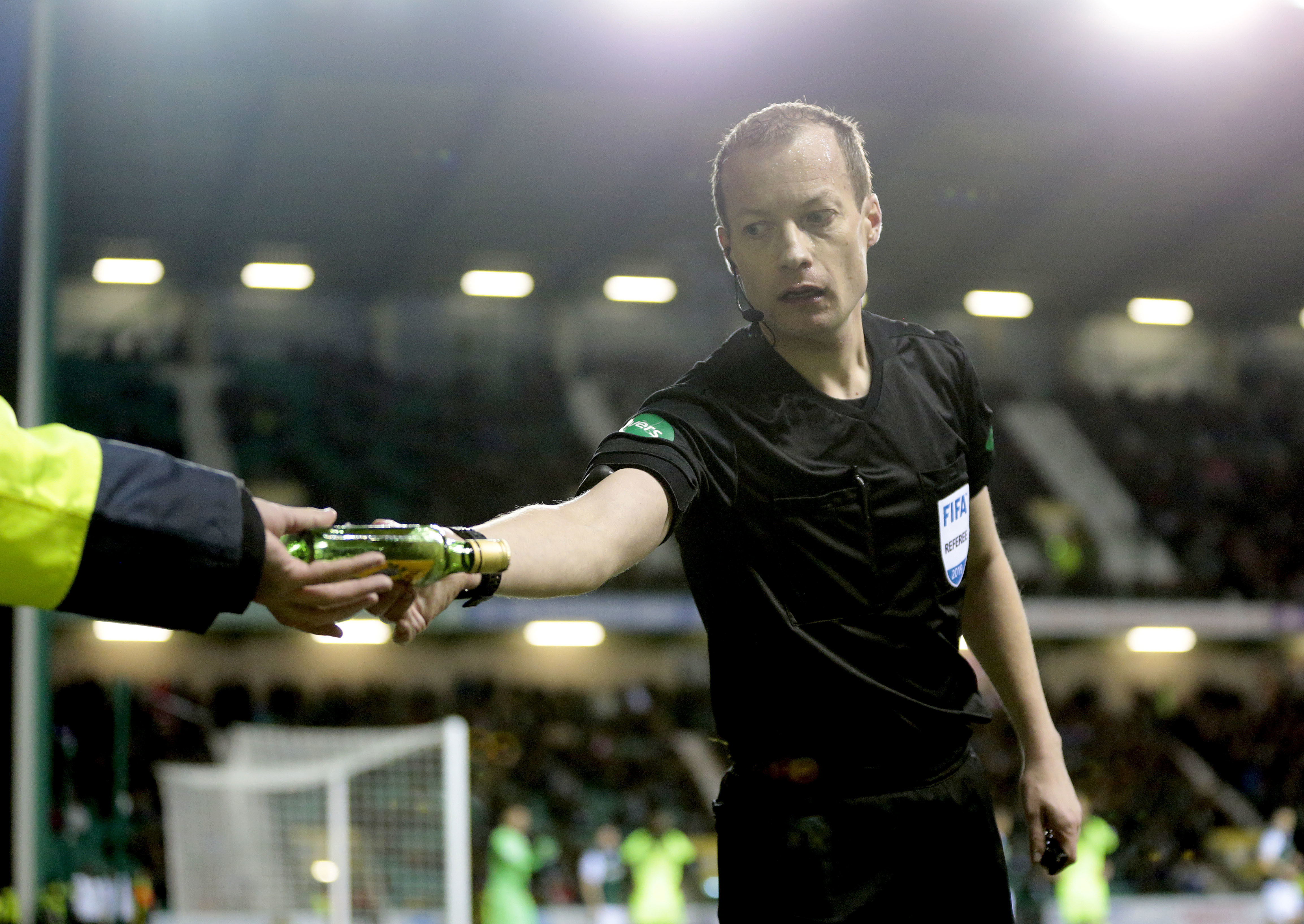 Referee Willie Collum removes a bottle from the Easter Road pitch after it was thrown at Celtic winger Scott Sinclair