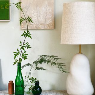 White lamp beside collection of coloured glass vases with ferns