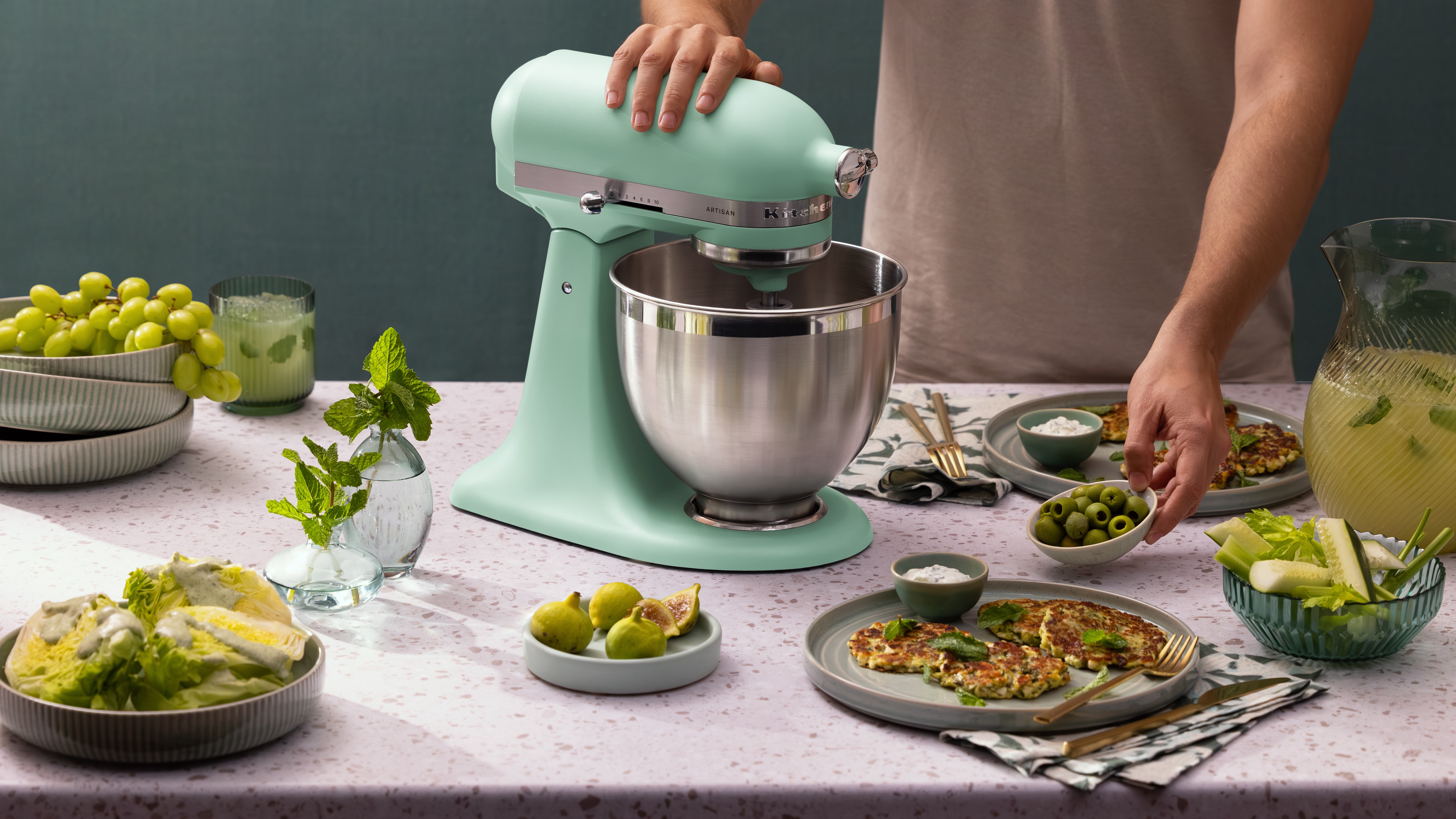 شخص يستخدم خلاط كيتشن إيد باللون النعناعي مع مجموعة مختارة من الأطعمة الخضراء على الطاولة