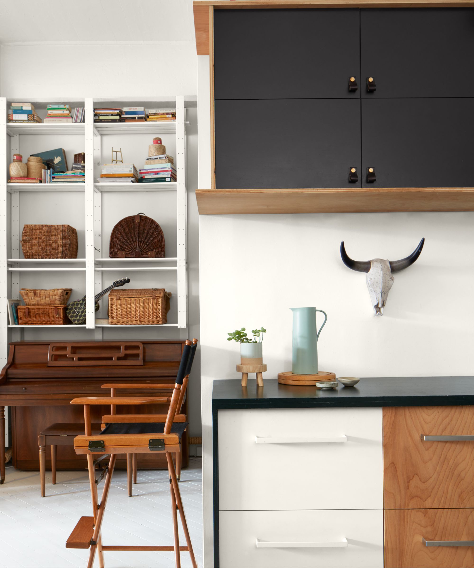 White and black kitchen with white open shelving housing baskets and decor, black cabinets, wooden chair, and black countertops