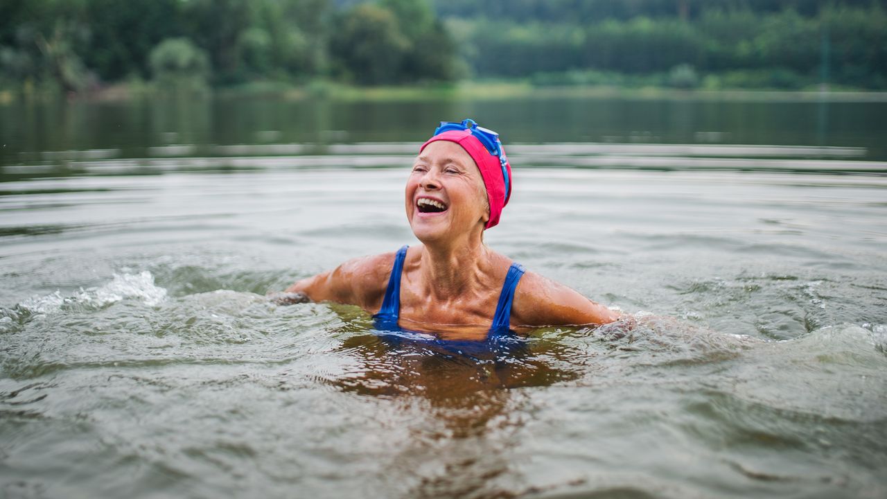 An older woman laughs as she&#039;s swimming in a mountain lake.