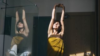 Woman reaching up and stretching after getting out of the shower in towel