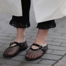 Close-up of black mesh Mary Jane flats styled with lace-trimmed black pants and a white coat.
