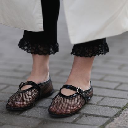 Close-up of black mesh Mary Jane flats styled with lace-trimmed black pants and a white coat.
