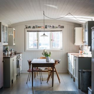 Purbeck Stone paint color by Farrow & Ball used in a small kitchen with cream cabinets, wall panelling and a midcentury modern dining table