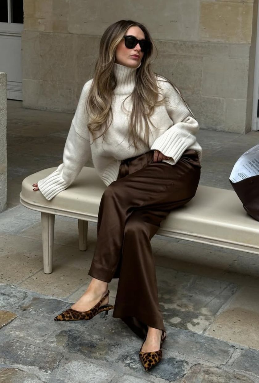 @oliviafaeh wears a cream high-neck jumper, brown satin trousers and leopard shoes