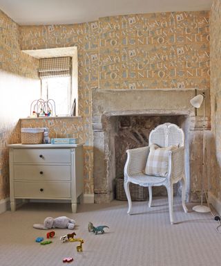 Gender neutral nursery with beige color scheme, alphabet printed buttermilk wallpaper and French style pale gray furniture.