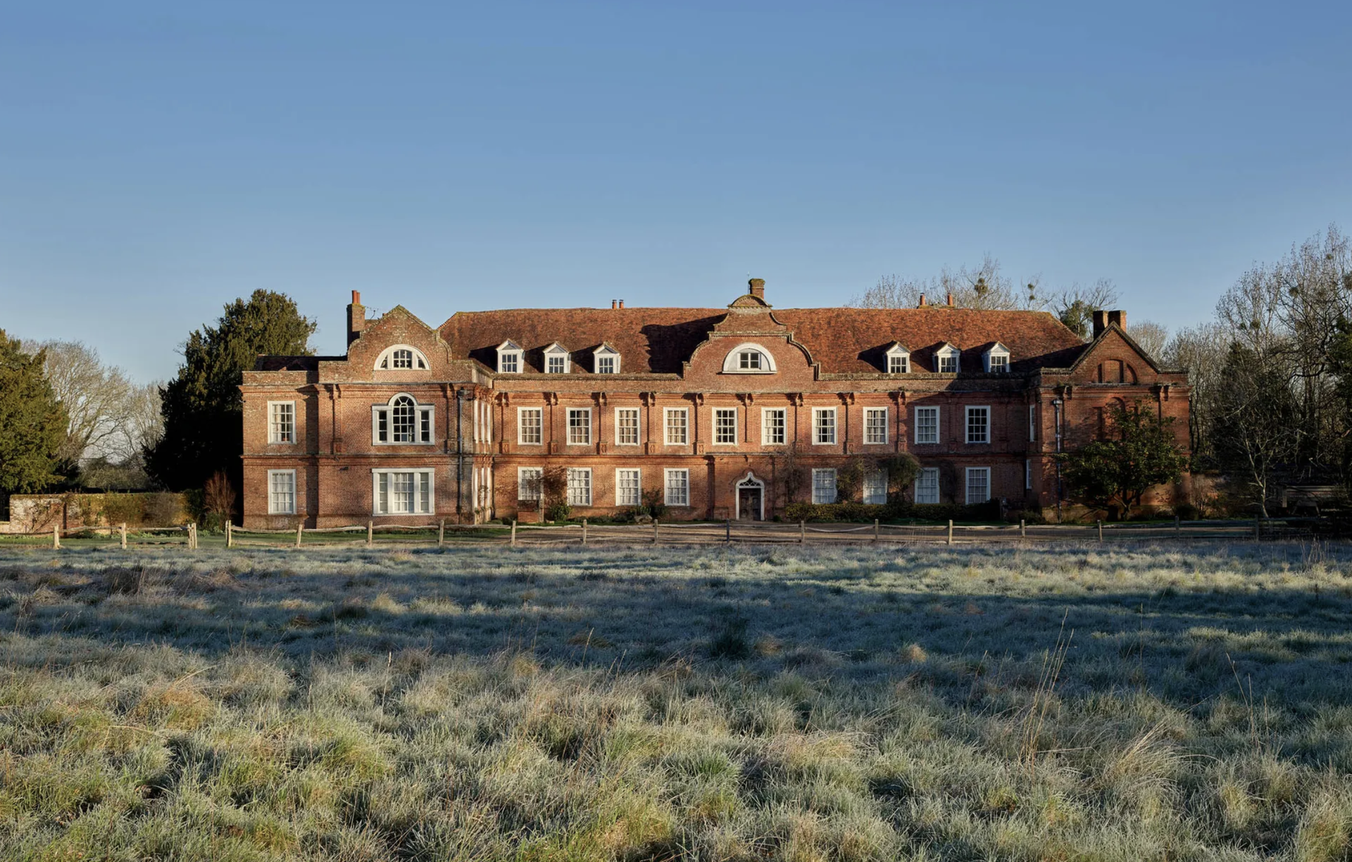 A view of West Horsley Place, which is red brick, three storeys high and very wide with two projecting wings