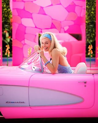 Margot Robbie as Barbie sitting in a pink convertible car