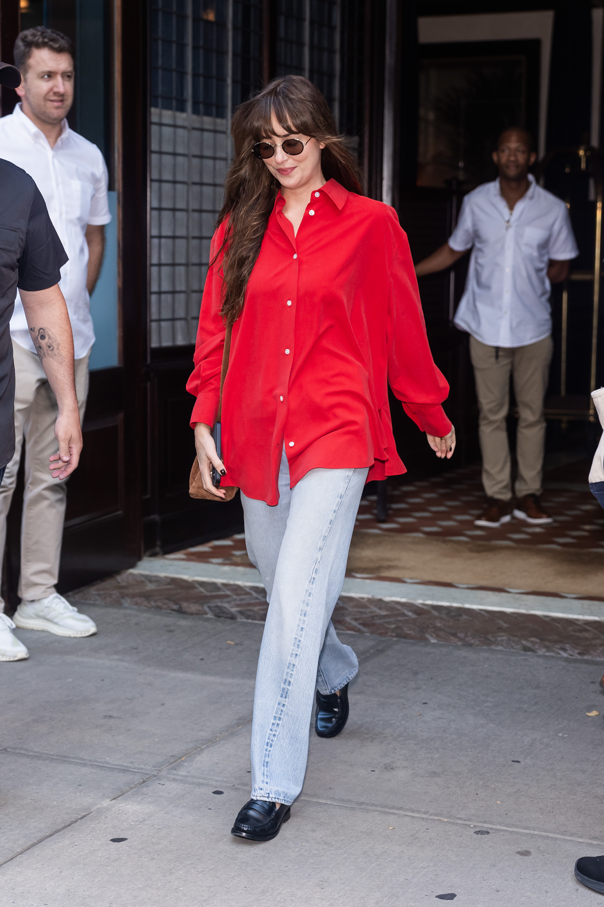 Dakota Johnson is in an oversized red button-down and pale Levi jeans.