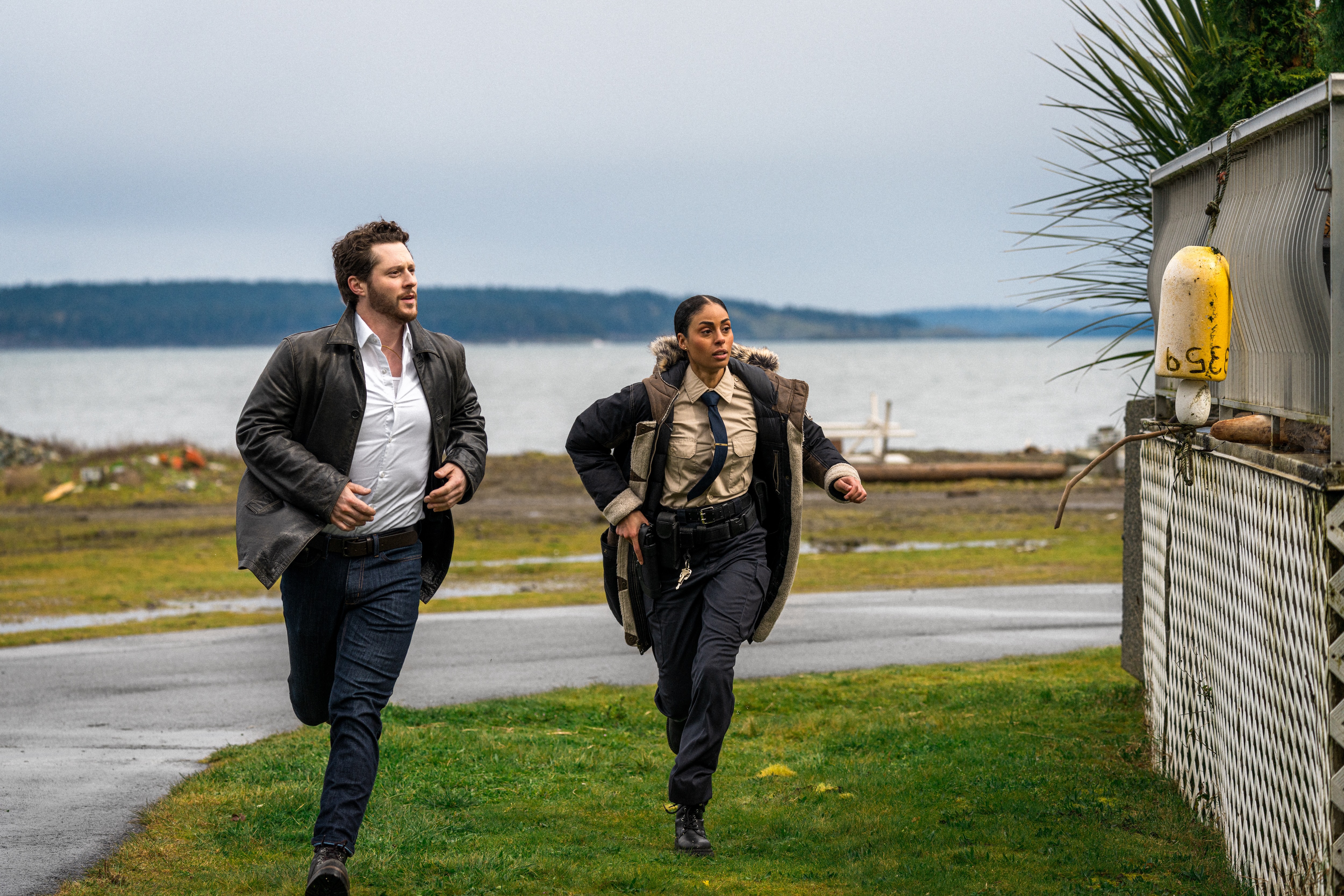 A man (Noah Reid) and a female cop (Clark Backo) run across the lawn of a lakeside home in the Crave TV show 'Yaga.'