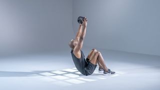 Man performing a dumbbell sit-up against grey backdrop