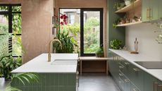 green kitchen with tiled island bench, plaster walls, and houseplants