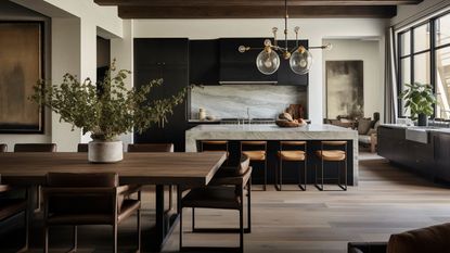 A large open plan kitchen with a marble island and four bar stools. The kitchen has black cabinets, a large light fixture, and wooden floors. There is a dining table with chairs on one side of the room.