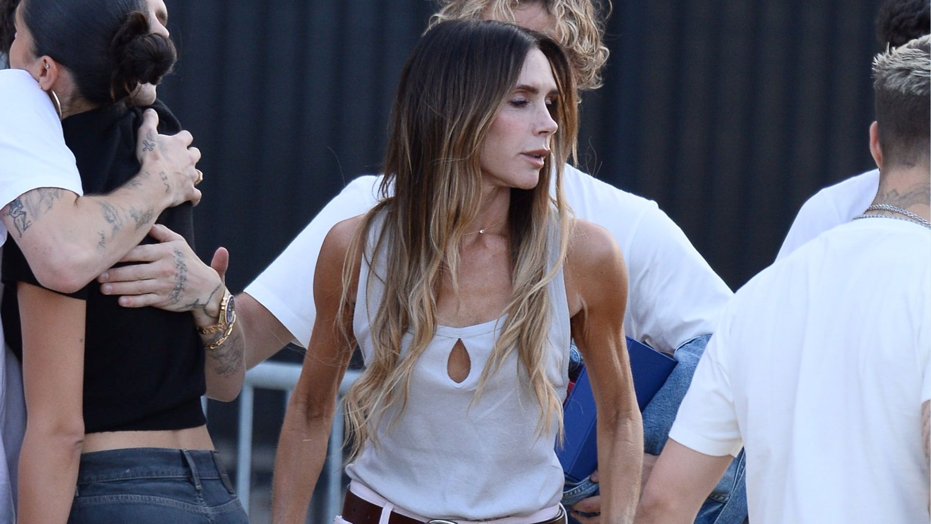 Victoria Beckham wears white straight-leg jeans with a cream vest top and brown leather belt.